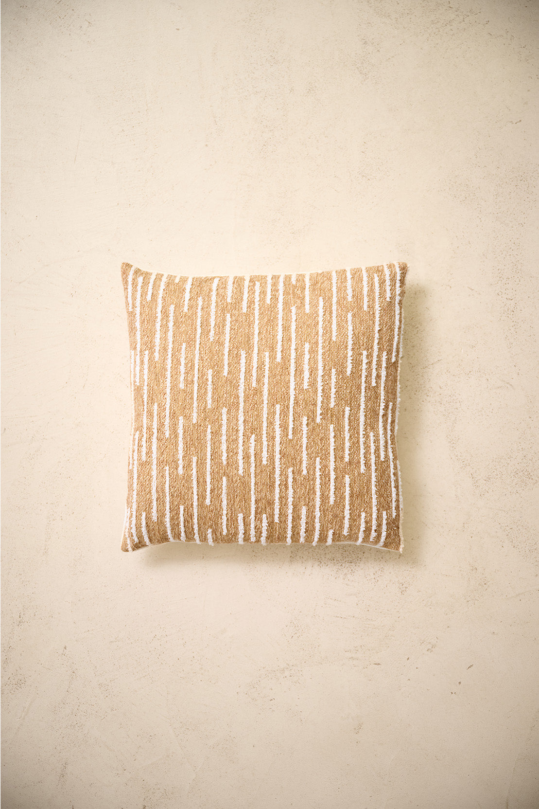 coussin carré CASTLE à chenille blanche sur marron ocre, sur un mur en enduit crème