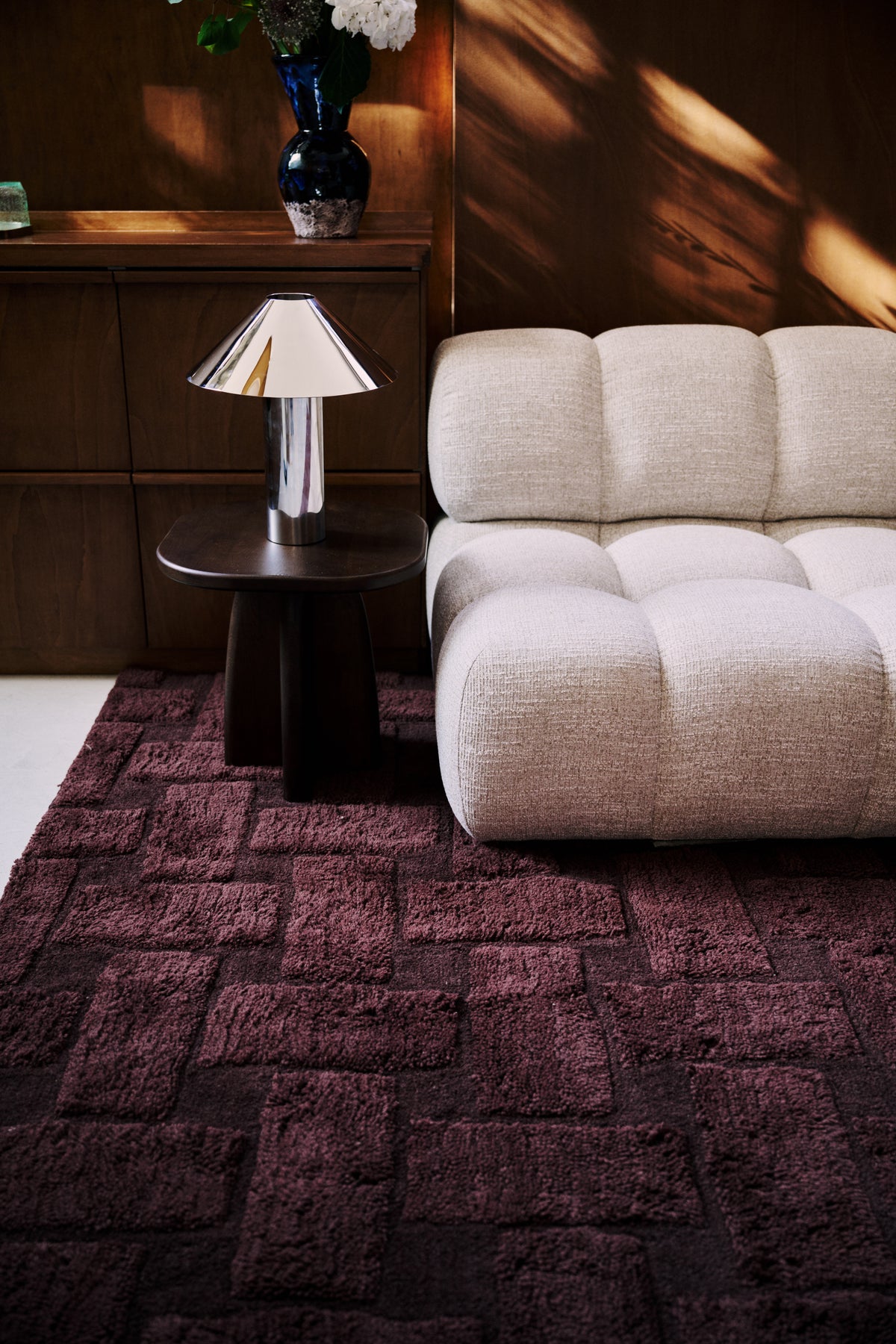 tapis de salon Woven bordeaux et son motif tressé au pied d'un canapé capitonné écru