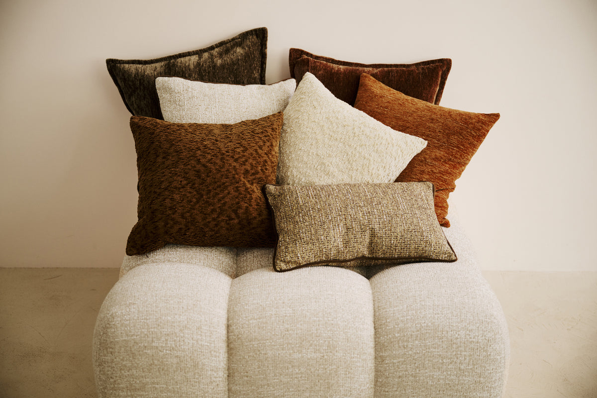 ensemble de coussins LODGE en velours, chenille et tweed posés sur un pouf en bouclé écru