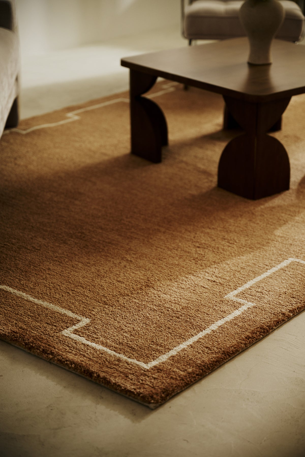 tapis de salon Crest caramel à motif à créneaux écru au pied d'un canapé en velours côtelé
