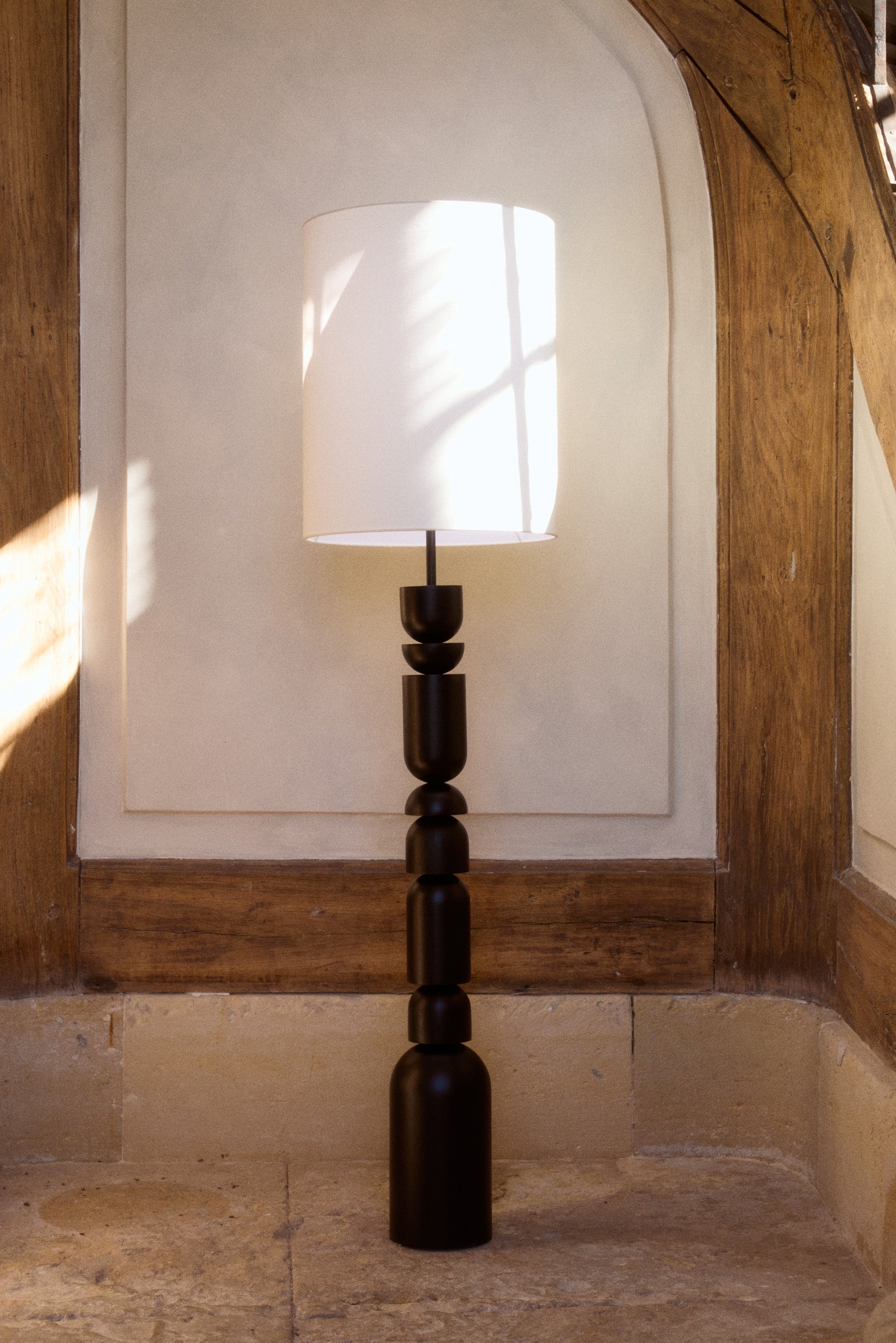 lampadaire Tinga - bois tourné noir et abat-jour lin blanc - vue de face alcôve pierre