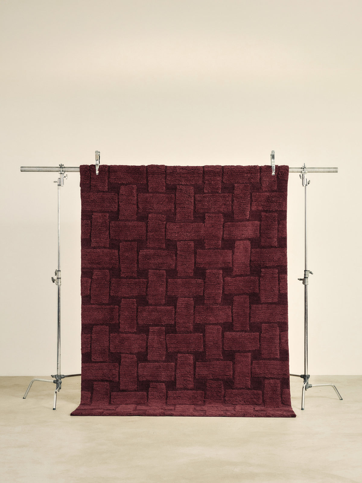 tapis de salon Woven bordeaux à motif tressé en relief suspendu sur un portant de studio