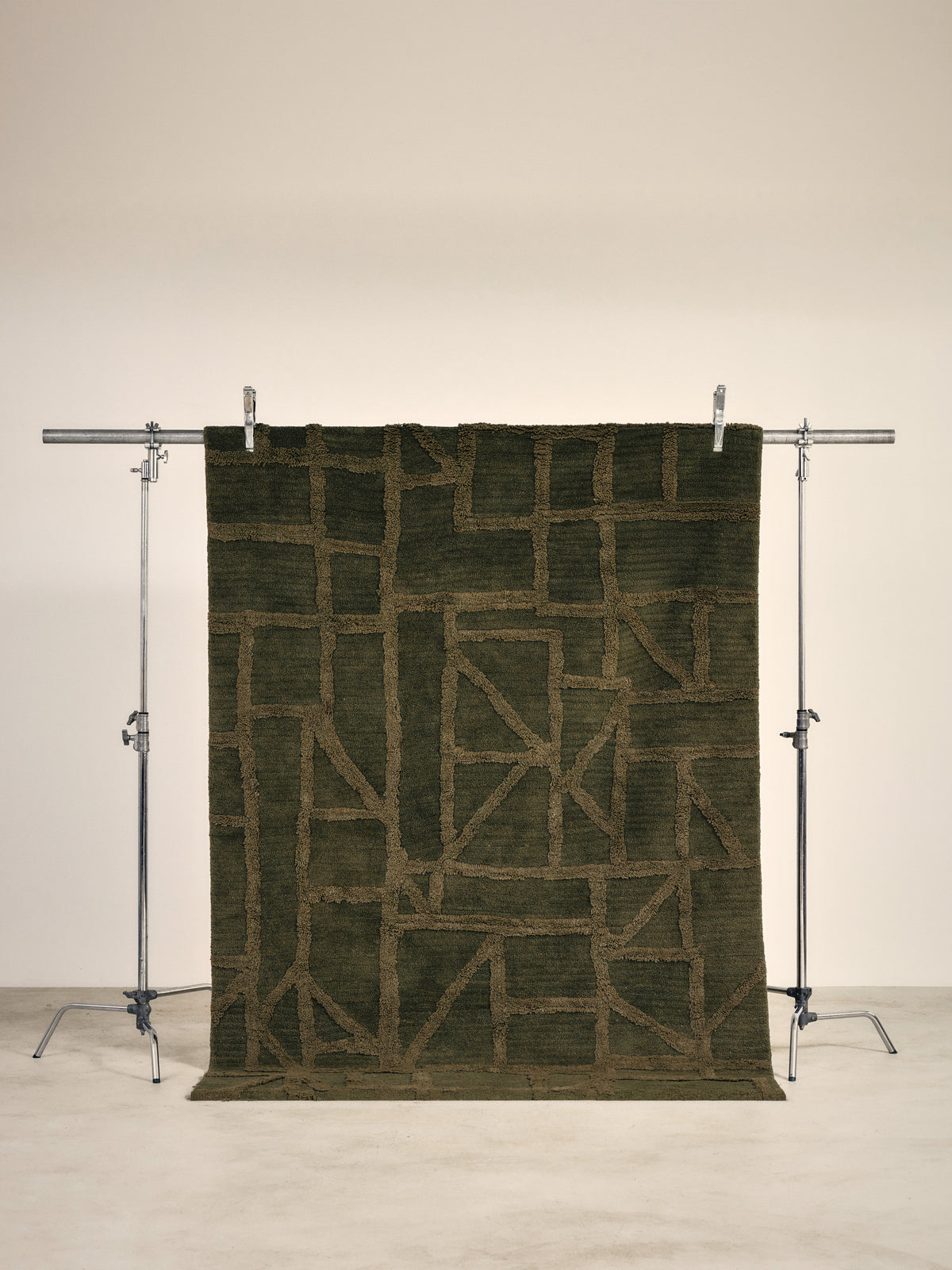 tapis de salon Strato vert kaki à motif géométrique en relief suspendu sur un portant