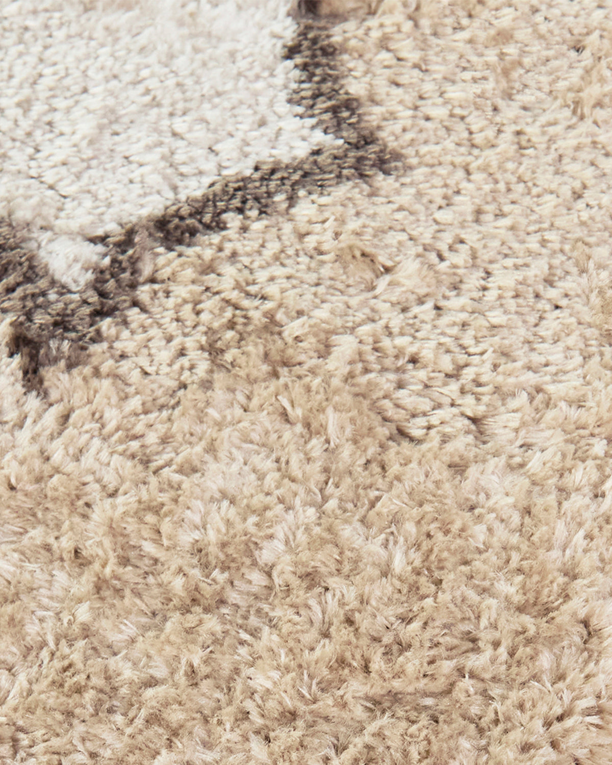 gros plan sur le liseré brun festonné et le velours épais écru et beige du tapis TIDAL