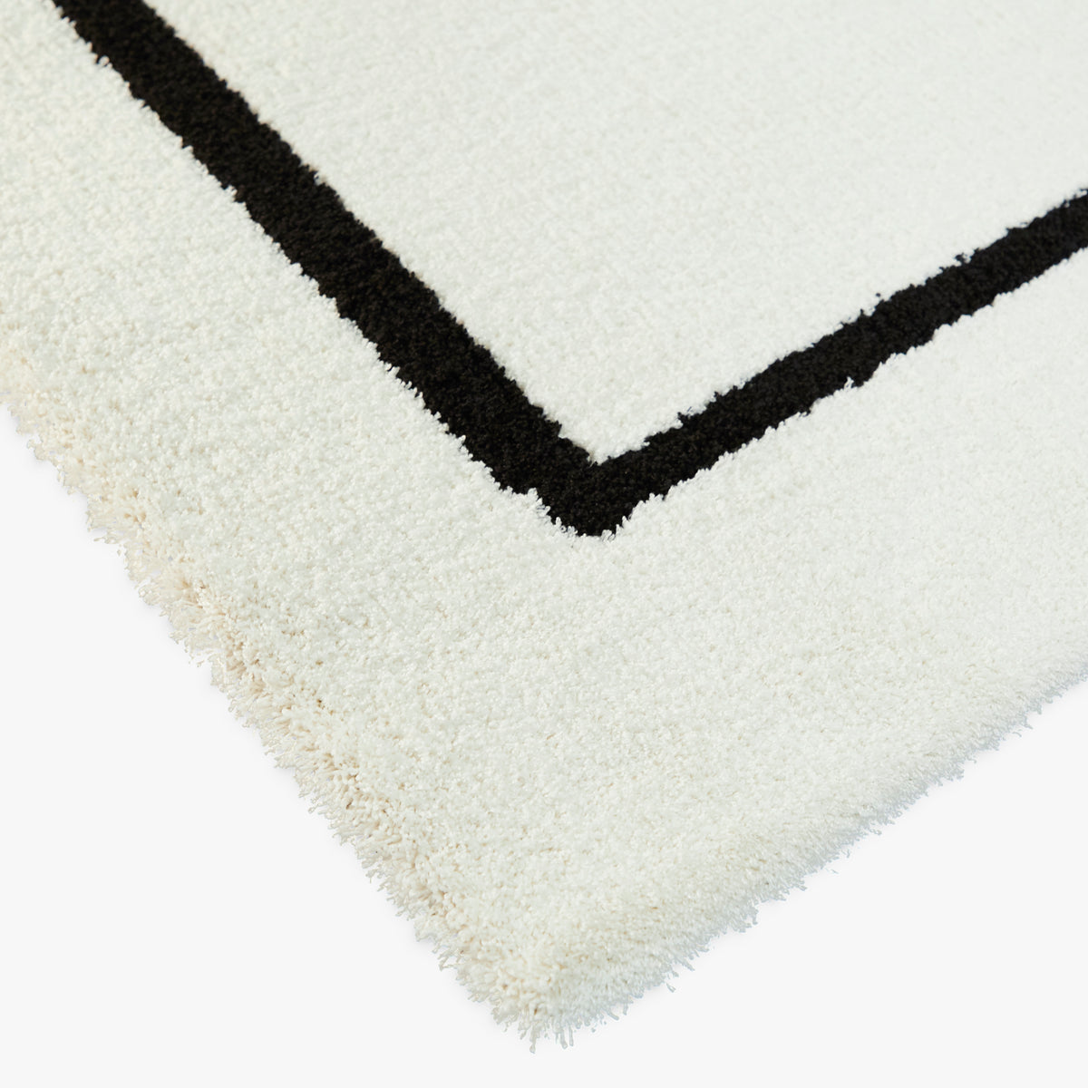 gros plan sur le velours ras écru du tapis ARCA et l'angle net d'un tracé noir épais