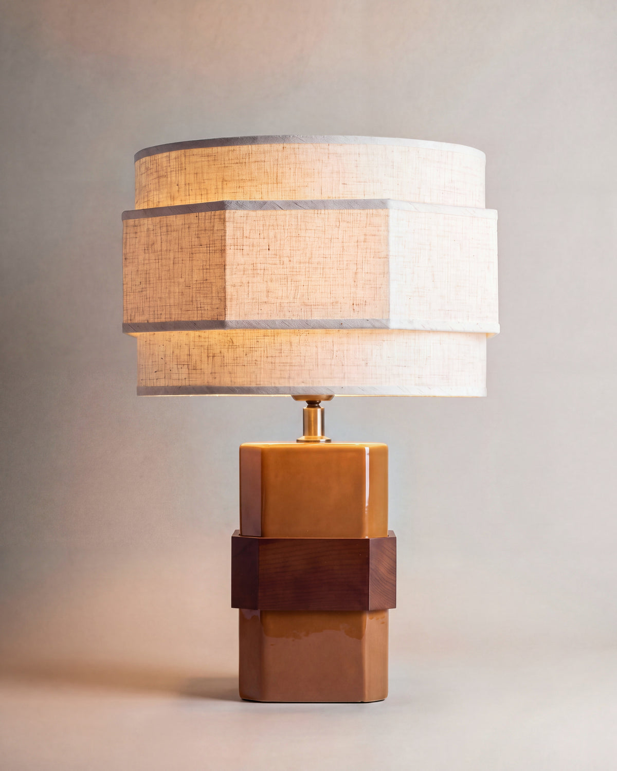 lampe de table EIRA allumée, pied en céramique ocre ceinturé de noyer, abat-jour à étages