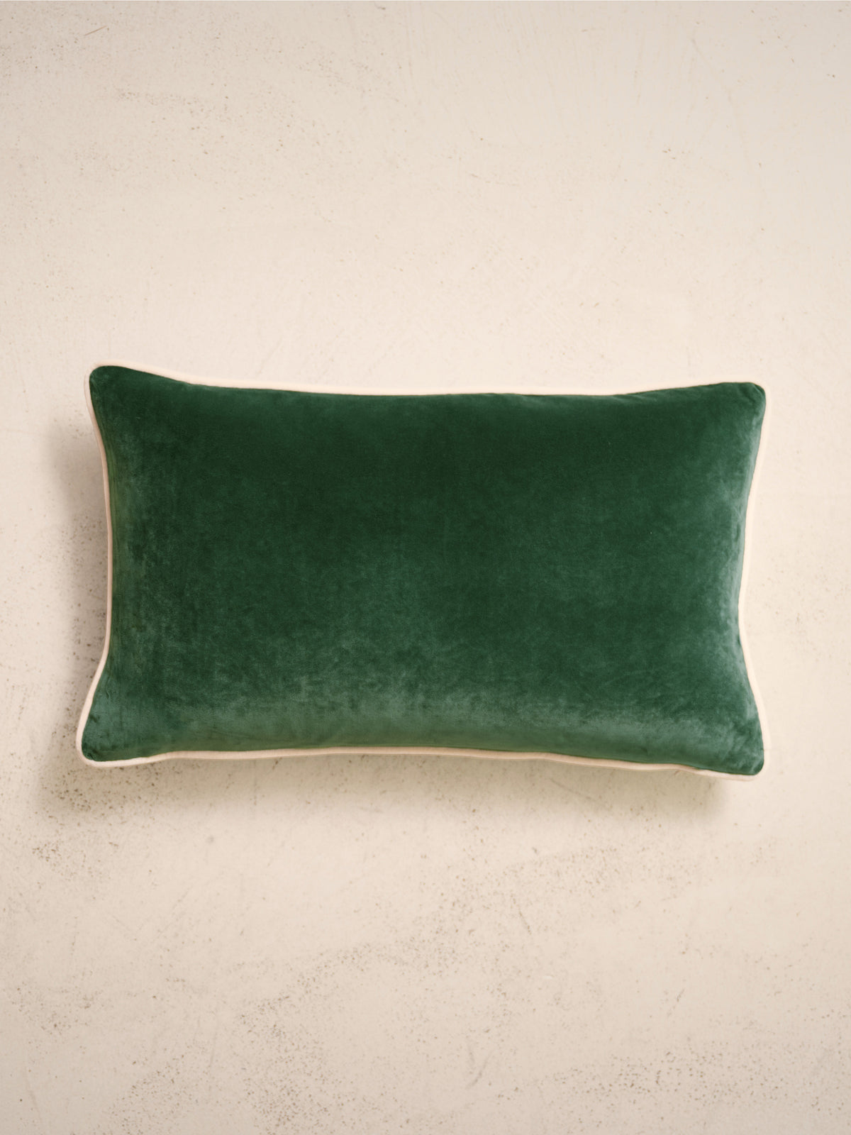 coussin rectangulaire LODGE en velours vert sapin à passepoil écru, sur un mur en enduit crème