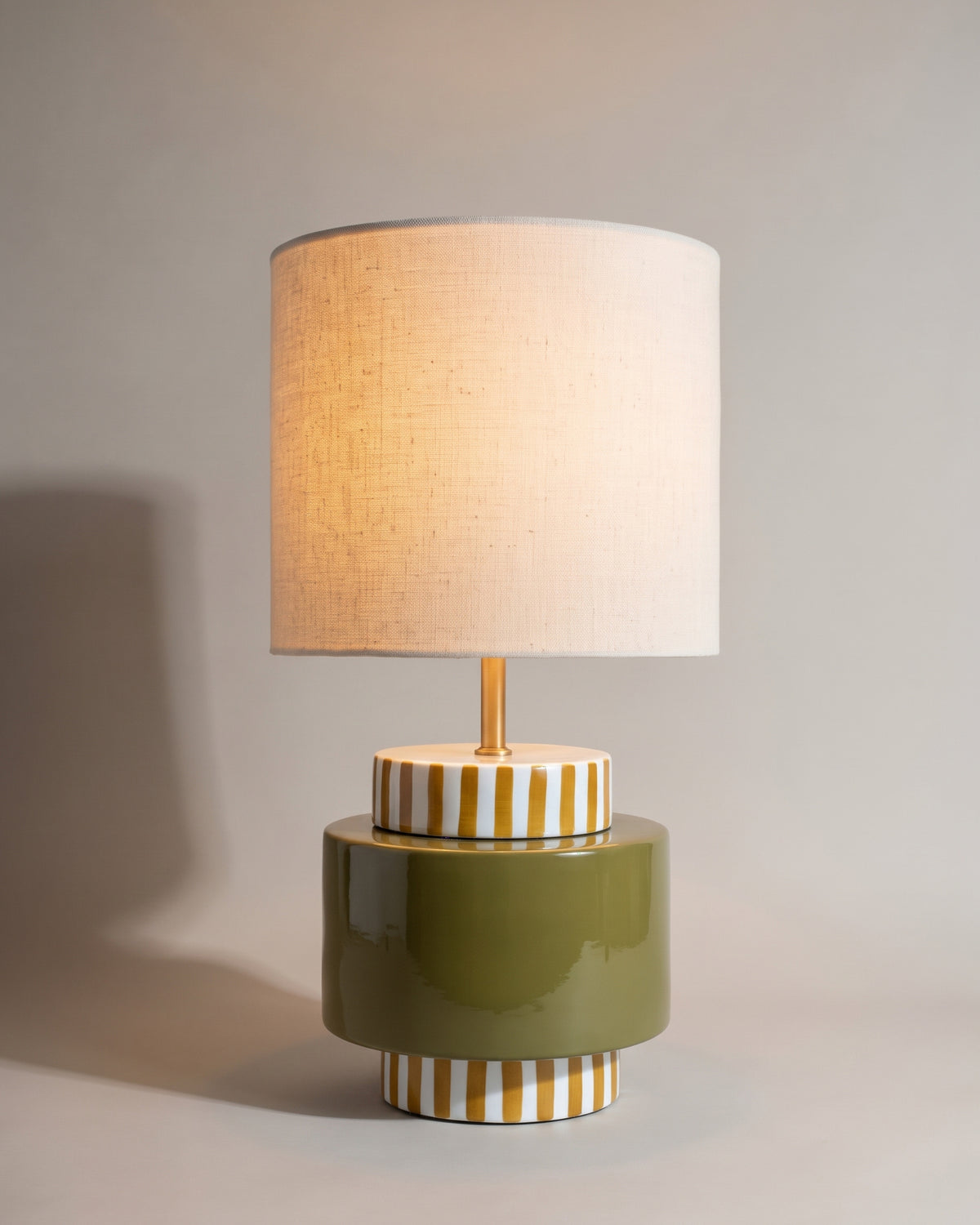 lampe de table ONJO allumée, pied en céramique vert olive à rayures jaunes et blanches