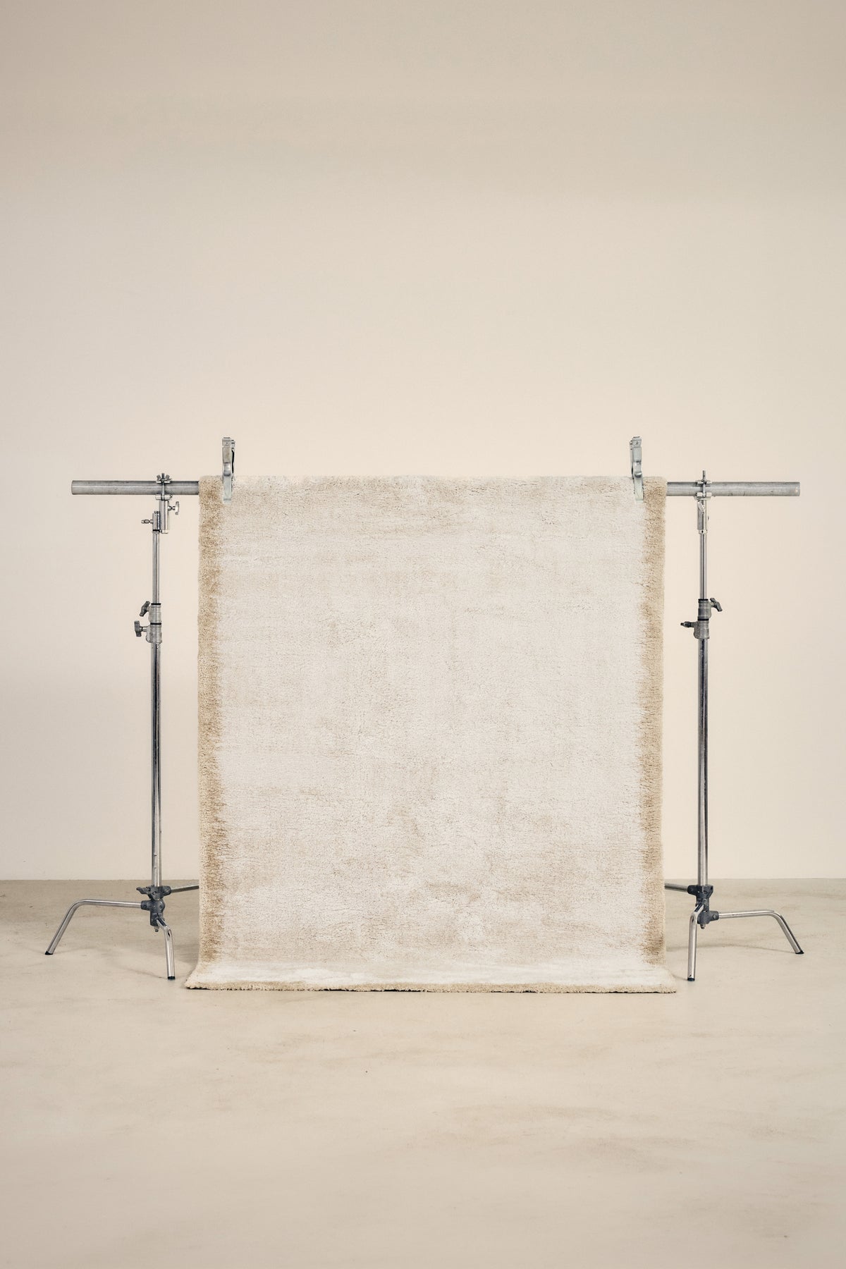 tapis SENNEN petit format, écru à bordure beige fondue, suspendu sur un portant de studio