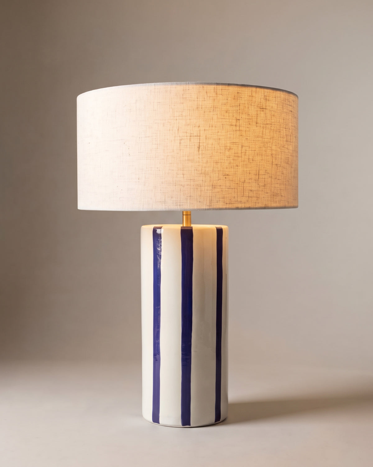 lampe de table ZHOE allumée, pied en céramique blanche à rayures bleu cobalt peintes