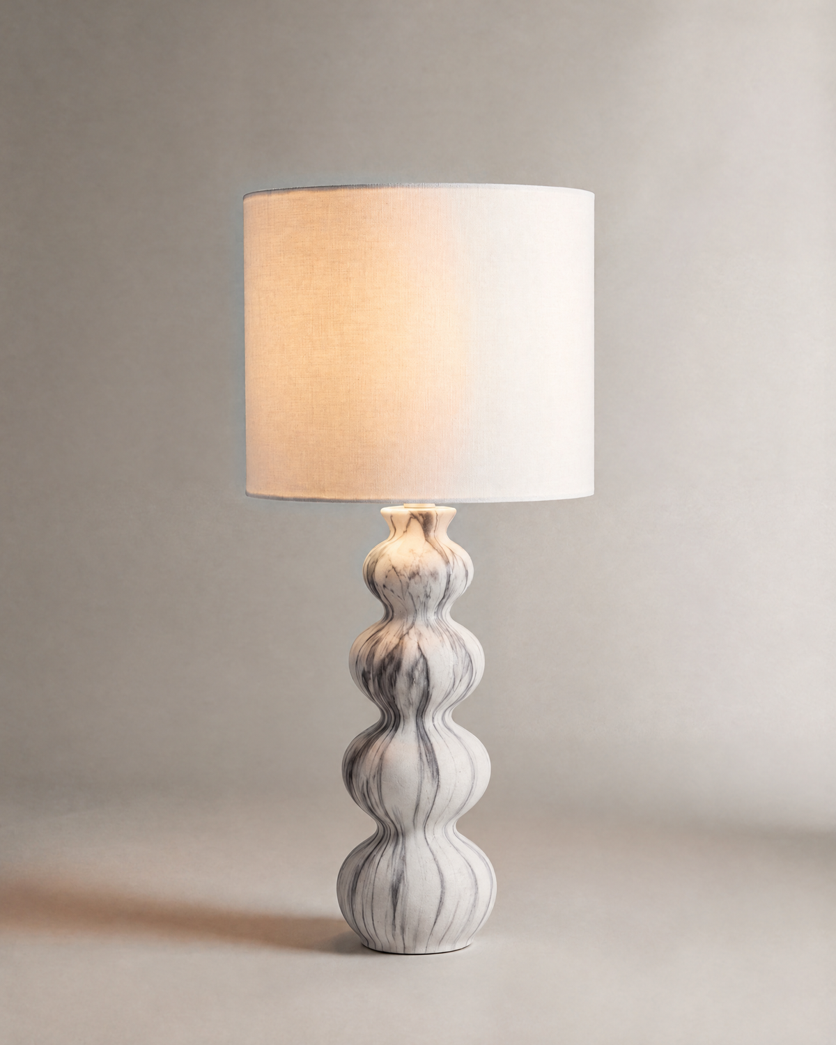 lampe de table NEBULA allumée, pied ondulé en céramique marbrée et abat-jour écru